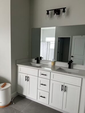 Un baño con muebles blancos, dos lavamanos, un espejo y una lámpara sobre el espejo.