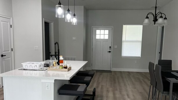 A modern kitchen with a central island, black bar stools, and pendant lighting. - Family Fun Getaway, Spacious, Cozy & Kid-Friendly (Ocala)