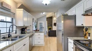Eine moderne Küche mit weißen Schränken, einem Edelstahl-Kühlschrank, einem Einbauofen und einer Arbeitsplatte aus Granit.
