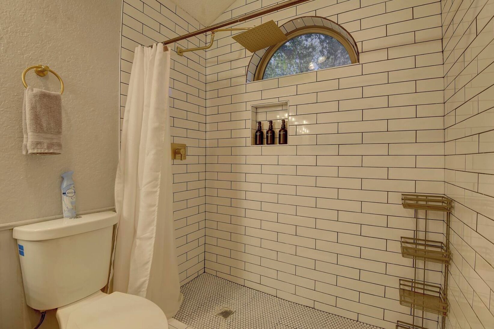 Un baño con azulejos blancos estilo metro, una ducha con puerta de cristal, inodoro y un ventanal pequeño.