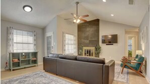Ein Wohnzimmer mit einer Couch, einem Fernseher, einem Deckenventilator und einem Kamin.