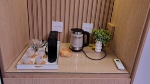 A compact kitchenette with a coffee maker, a kettle, and a small plant on a wooden countertop.