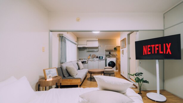 A modern hotel room with a bed, a sofa, a small table, and a TV displaying "NETFLIX". - Showa Bloom · Near Shinjuku Station (Tokyo)