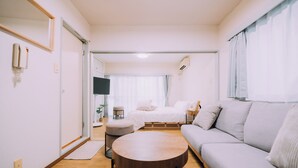 A modern living room with a sofa, a round coffee table, a TV, and a bed with a window view. - Showa Bloom · Near Shinjuku Station (Tokyo)
