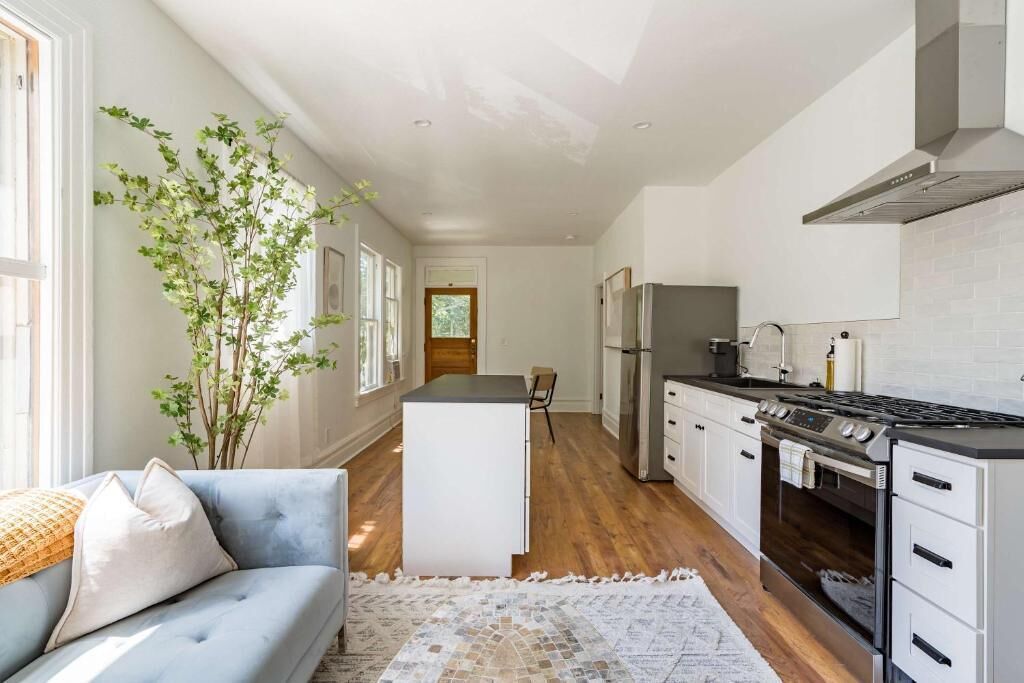 A modern kitchen with white cabinetry, a central island, and a dining area with a sofa and a plant.