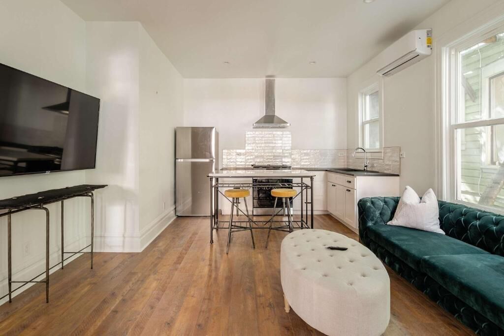 A modern kitchen with a stainless steel refrigerator, a bar stool setup, and a green upholstered sofa.