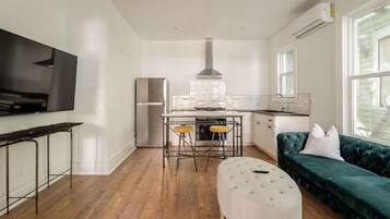 A modern kitchen with a stainless steel refrigerator, a bar stool setup, and a green upholstered sofa.