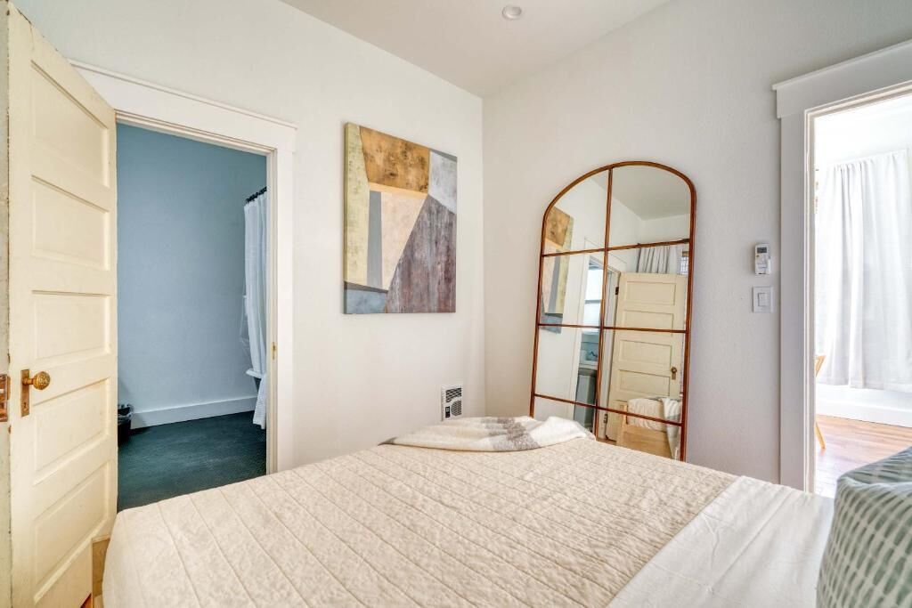 A bedroom with a bed, a mirror, a door, and a painting on the wall.