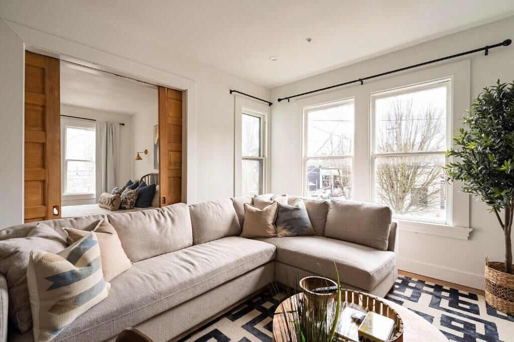 A living room with a beige sectional sofa, a patterned rug, and a large window with a view of trees.