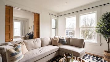 A living room with a beige sectional sofa, a patterned rug, and a large window with a view of trees.