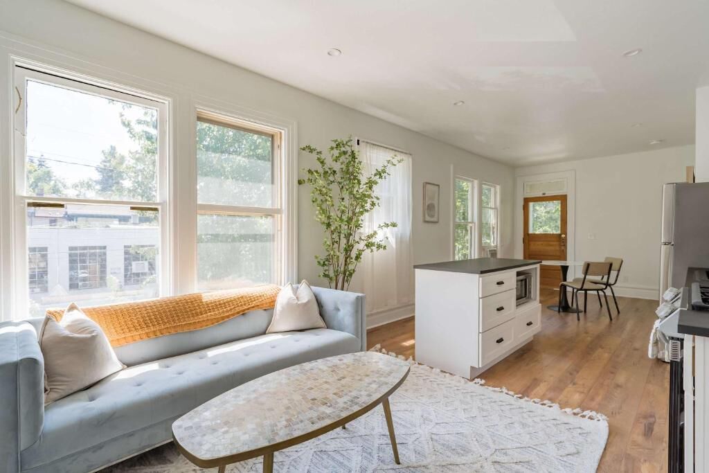 A modern living room with a sofa, coffee table, and a kitchen area with a refrigerator and cabinets.