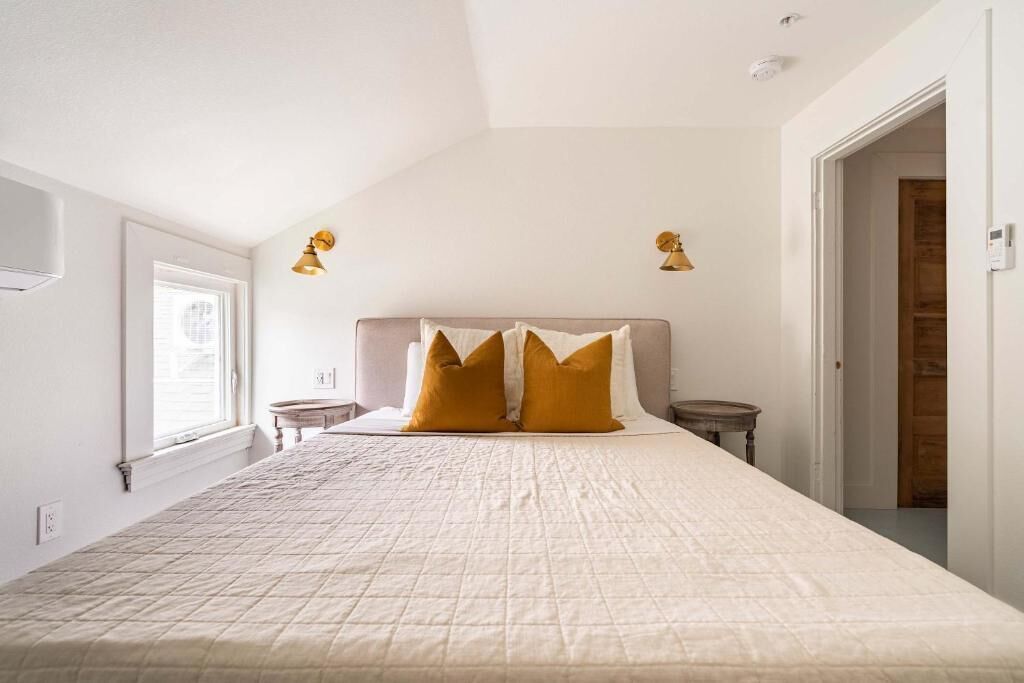A bedroom with a large bed, two bedside tables, a window, and two wall-mounted lamps.