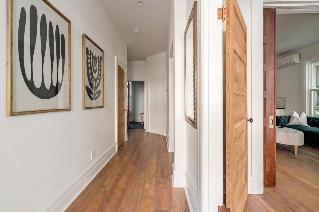 Un couloir doté d’un plancher en bois, de murs blancs et d’œuvres d’art encadrées.