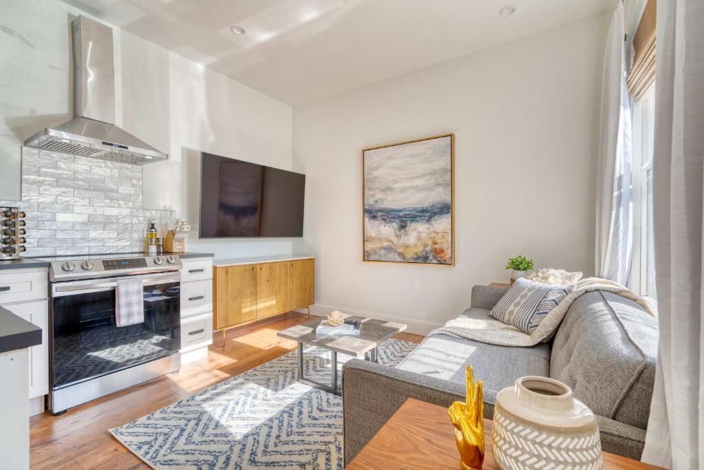 A modern kitchen with a built-in oven and a large stove, a dining area with a table and chairs, a sofa, and a painting on the wall.
