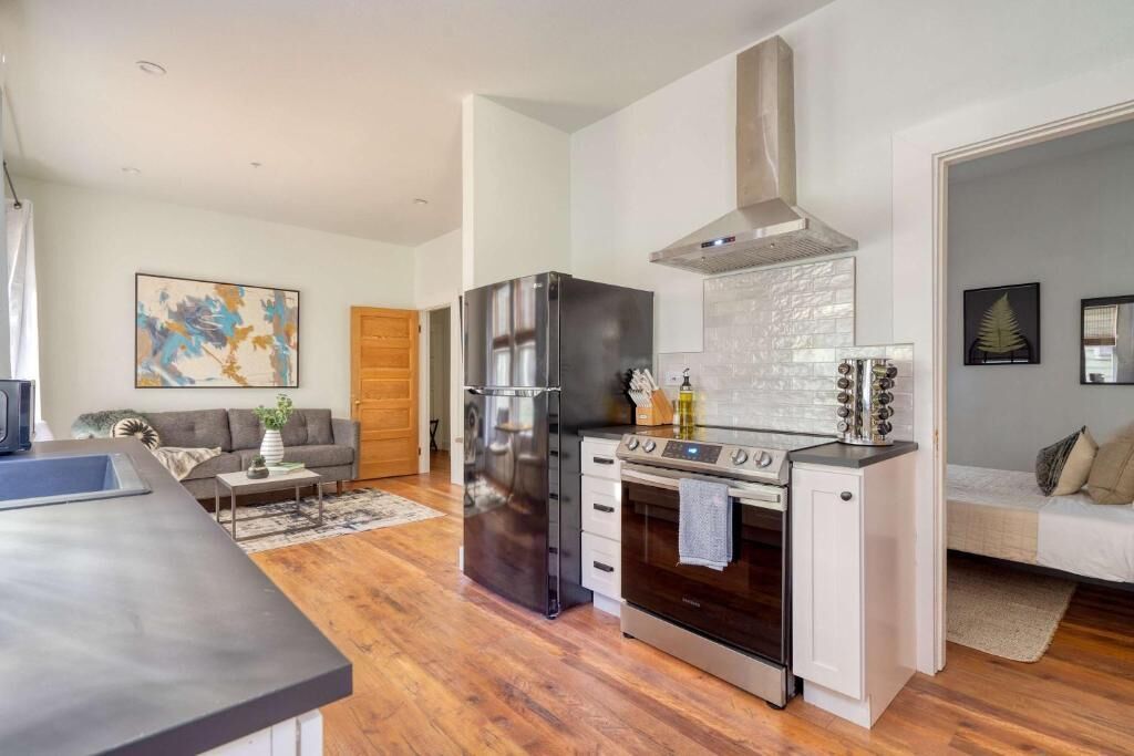 Une cuisine compacte équipée d’un réfrigérateur, d’un four et d’une cuisinière, un coin repas avec une table, et un salon avec un canapé et un tableau.