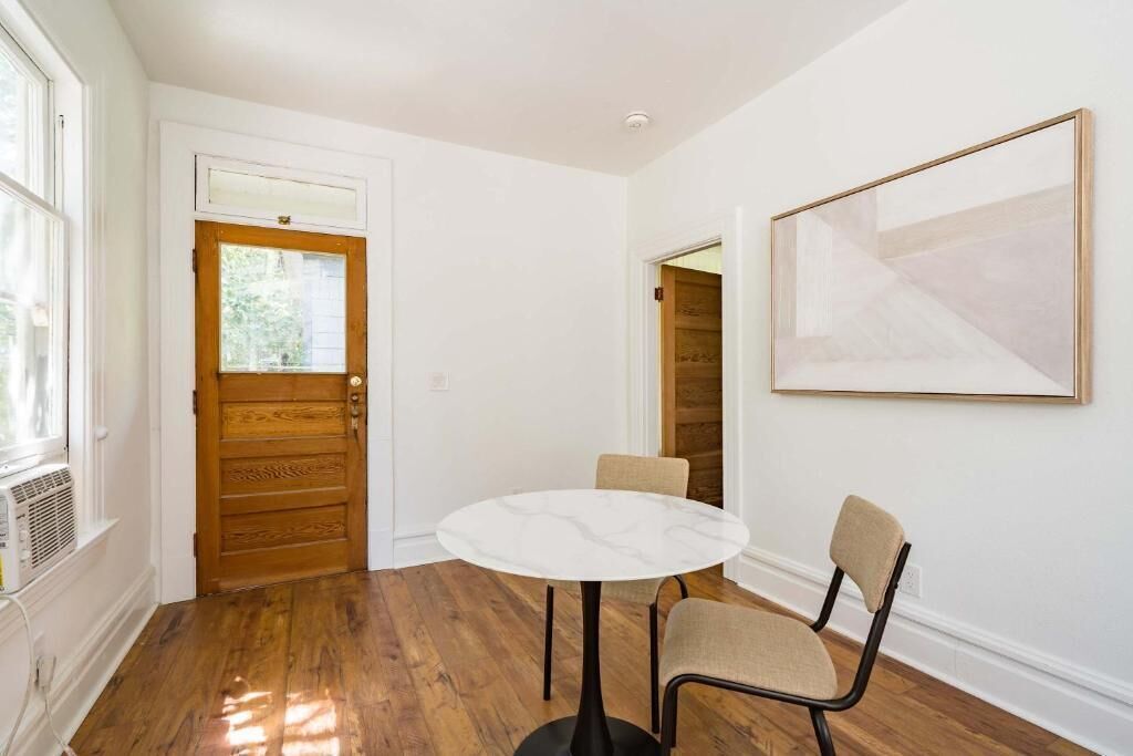A room with a wooden door, a round table with two chairs, and a large abstract painting on the wall.