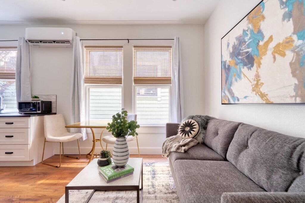 A modern living room with a sofa, a coffee table with a book and a plant, a desk with a chair, and a large abstract painting on the wall.