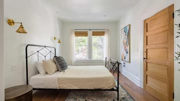 A bedroom with a bed, a window with blinds, a door, and a wall-mounted light fixture.