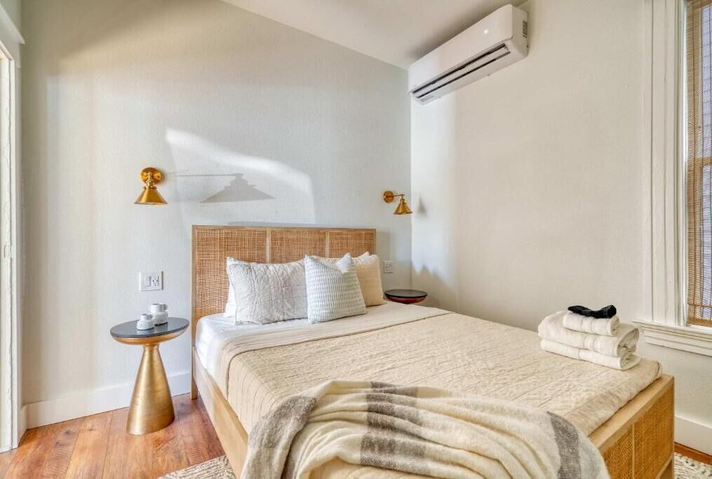 Een slaapkamer met een bed, nachtkastjes, een airconditioner en een raam.
