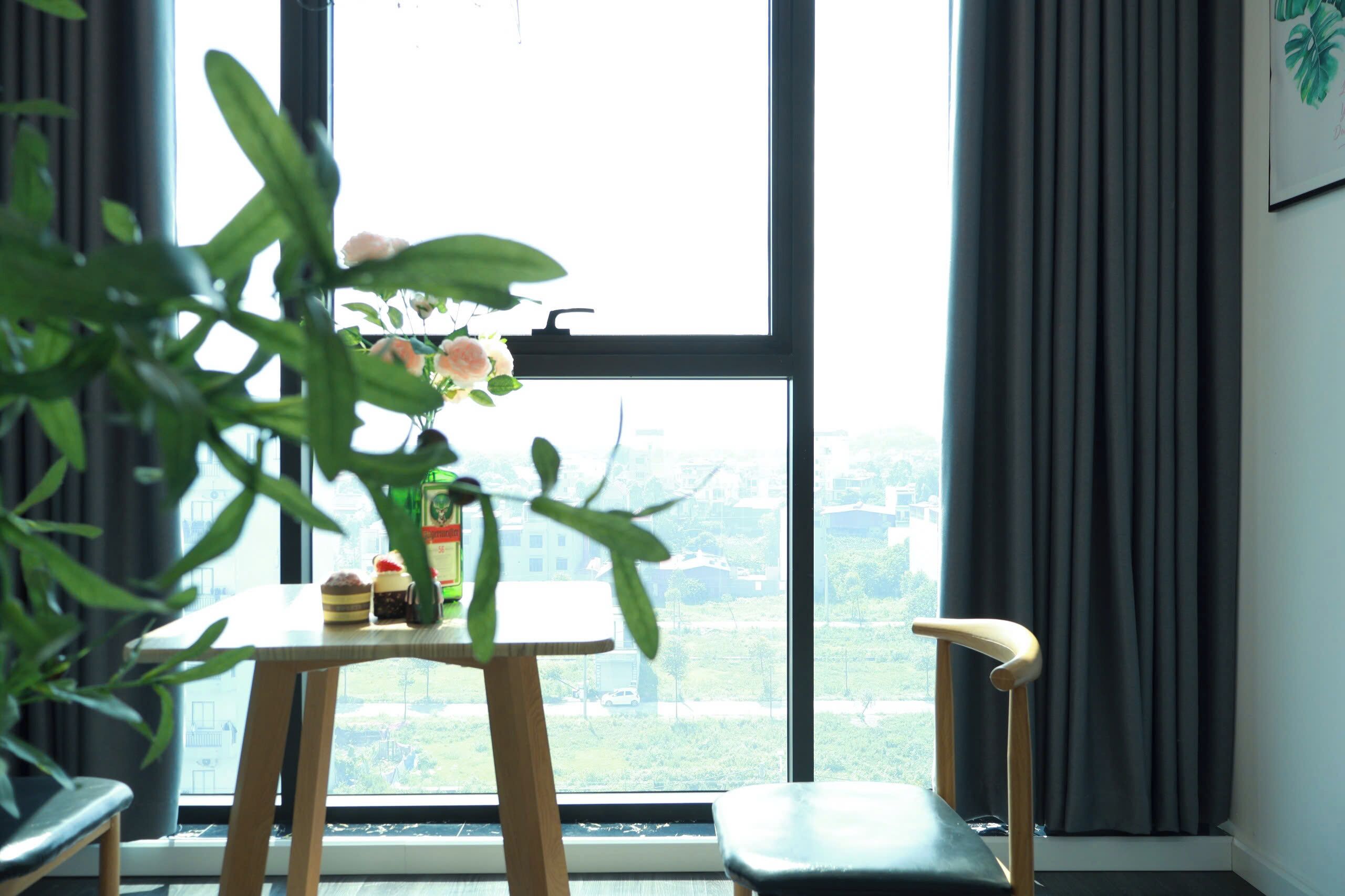 Una habitación con un ventanal grande, una mesa con un jarrón de flores, una silla y vistas a la vegetación exterior.