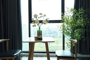 A room with a table by a window, a chair, a potted plant, and a bottle of liquor. - The Grand Diamond C Hotel (Nenh)