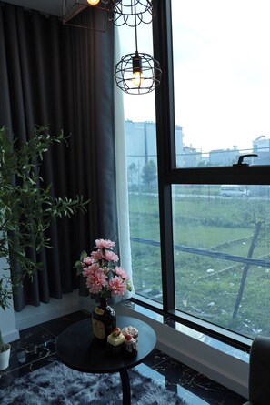 A room with a large window, a potted plant, a table with a vase of flowers, and a bottle. - The Grand Diamond C Hotel (Nenh)