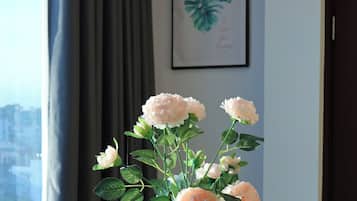 A room with a view of a cityscape, a vase of artificial flowers, and a basket of bread on a table.