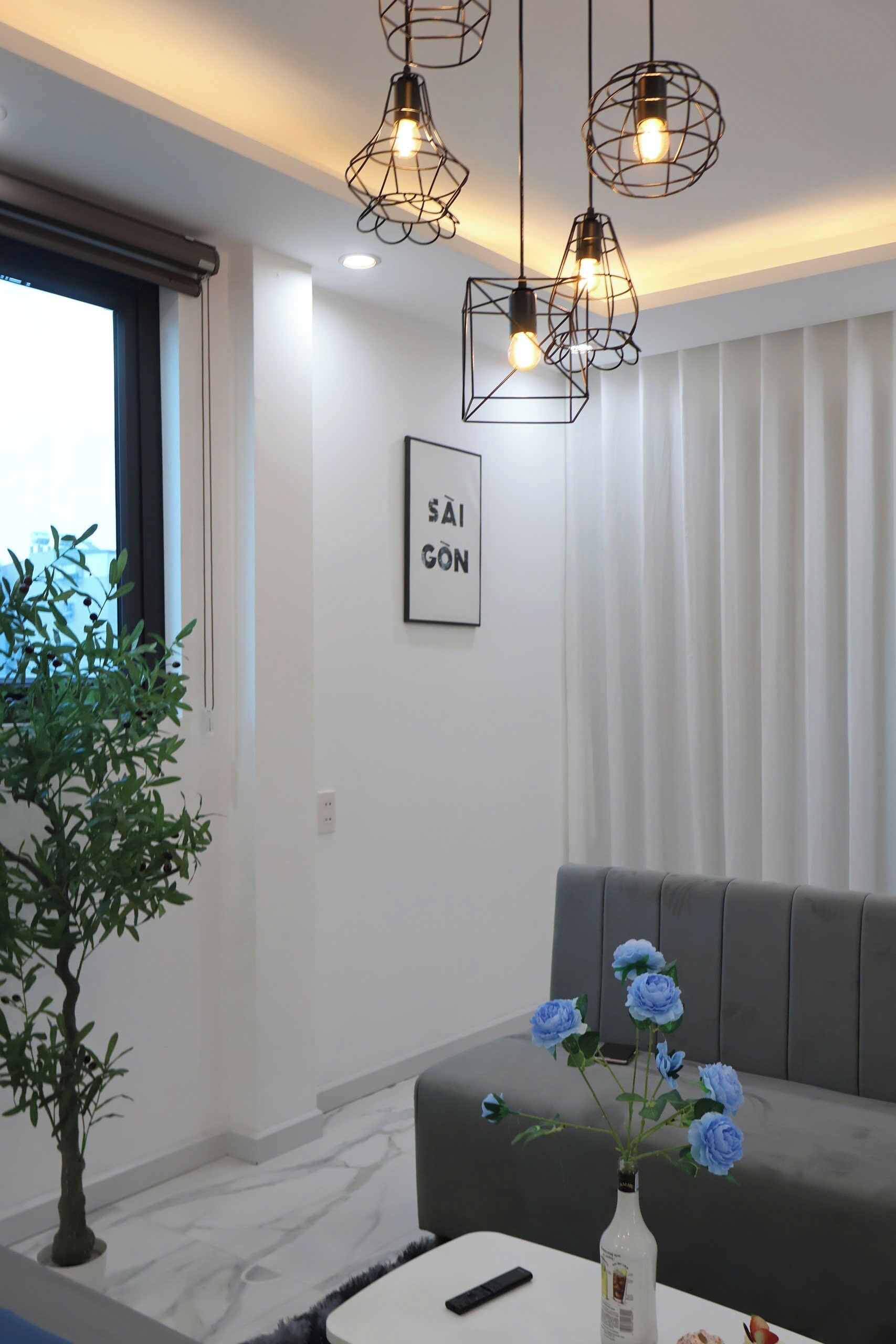 A modern living room with a grey sofa, a small table with a vase of blue flowers, and a framed picture on the wall.
