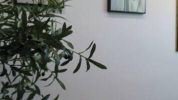 Een kamer met een grote groene plant, twee kunstwerken in lijsten aan de muur en een broodmandje op een zwart bijzettafeltje.