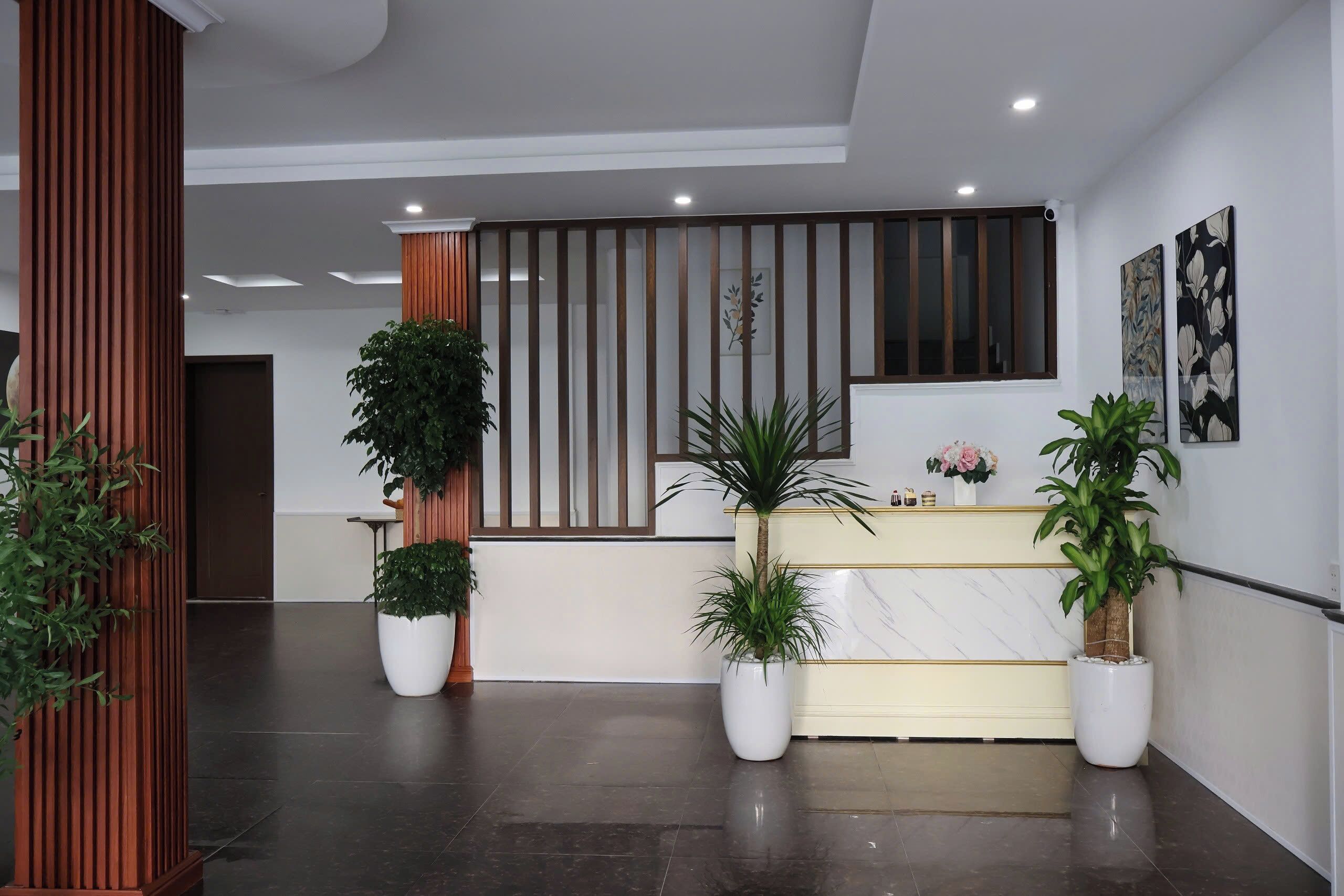A reception area with a modern design, featuring a reception desk, potted plants, and artwork on the walls.