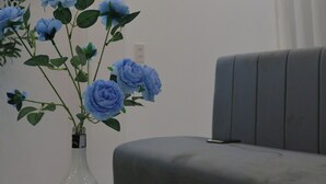 A modern living room with a grey sofa, a white table with a vase of blue flowers, and a framed sign on the wall. - The Grand Diamond C Hotel (Nenh)