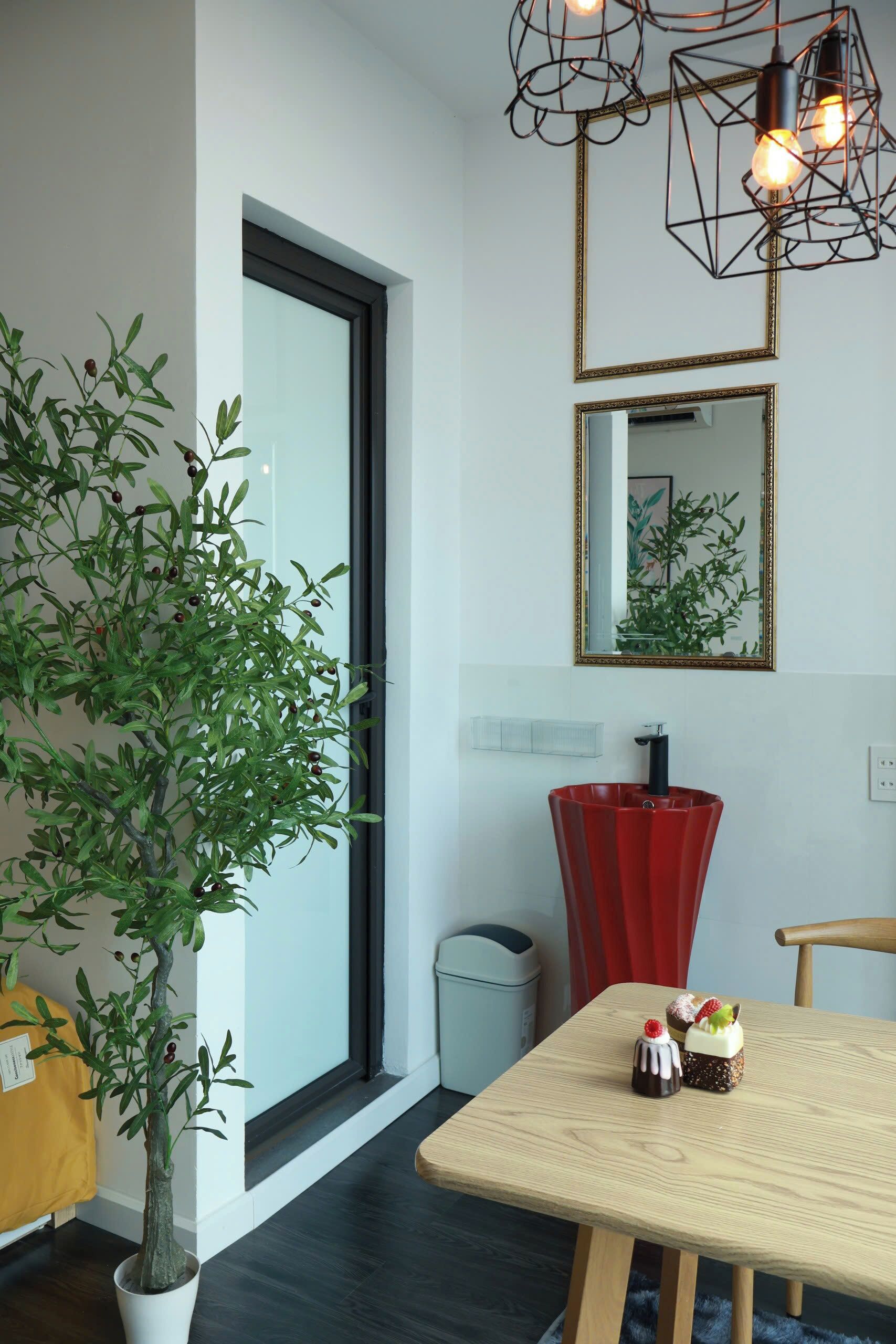 A modern interior with a potted plant, a red vase, and a table with two desserts.