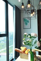 Una habitación con un ventanal grande, una cesta de mimbre con pan y pasteles, un florero con flores y una obra de arte enmarcada en la pared.