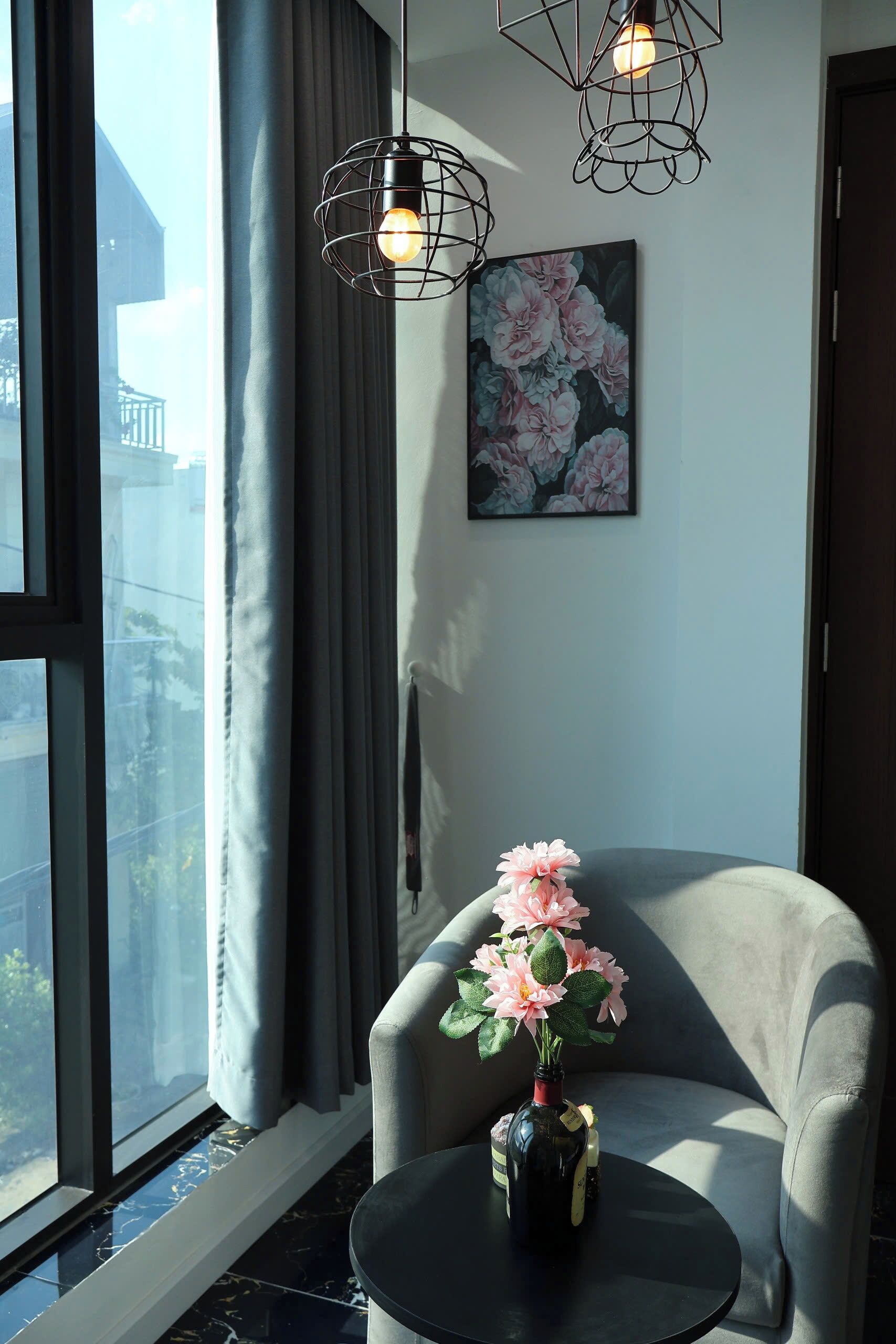 Et værelse med et stort vindue, en stol, et lille bord, en vase med blomster og et billede på væggen.