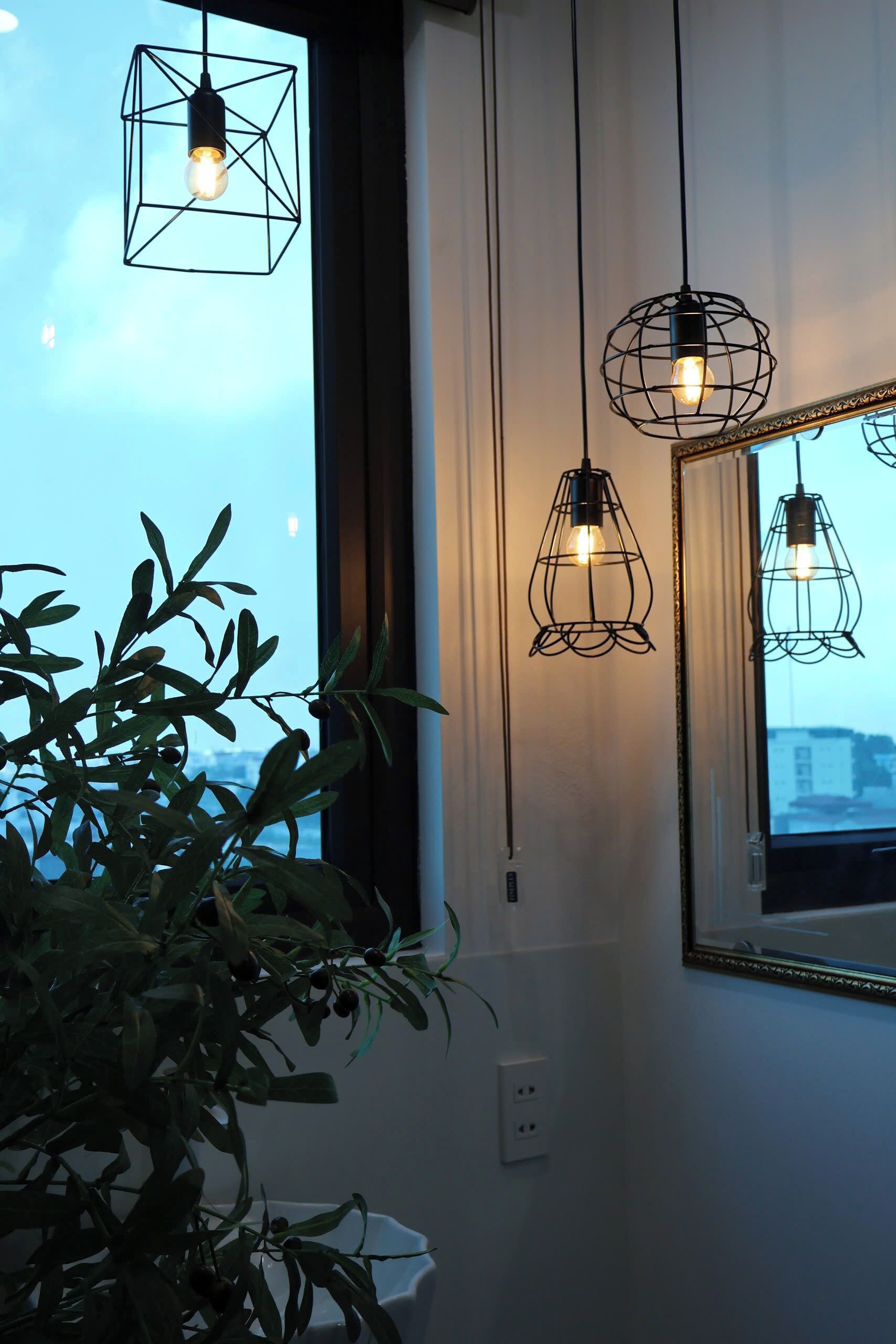 A room with a large window, a potted plant, and three hanging light fixtures.