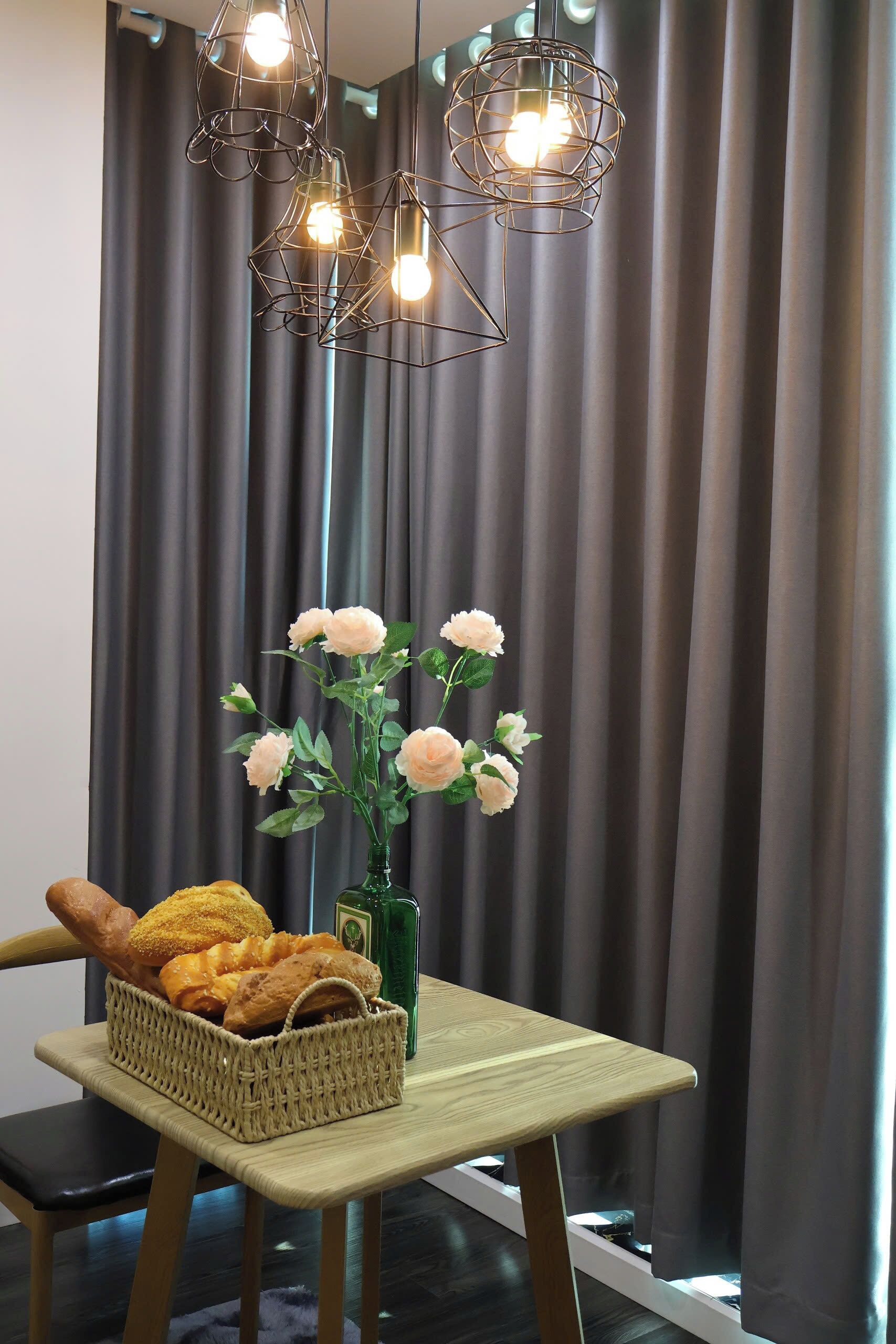 A table with a wicker basket of bread, a green vase with flowers, and a wooden chair.
