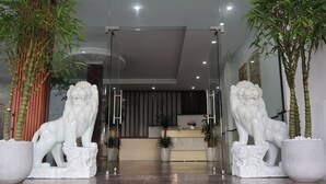 A reception area with two white lion statues flanking the entrance, a reception desk, and potted plants. - The Grand Diamond C Hotel (Nenh)