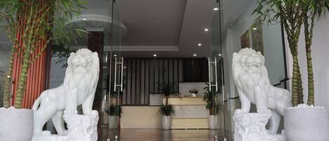 A reception area with two white lion statues flanking the entrance, a reception desk, and potted plants.
