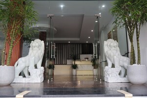 Zona de recepción con dos estatuas de leones blancos a ambos lados de la entrada, un mostrador de recepción y plantas en macetas.