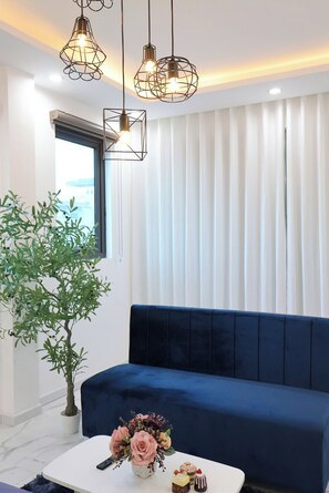 A modern living room with a blue sofa, a white coffee table with a vase of flowers, and hanging pendant lights. - The Grand Diamond C Hotel (Nenh)