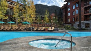 A hotel pool area with lounge chairs, a hot tub, and a mountain backdrop.