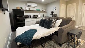 A compact living space with a bed, a sofa, a small table, and a kitchenette area. - Orbital Oasis: Dual Living near NASA (Baytown)