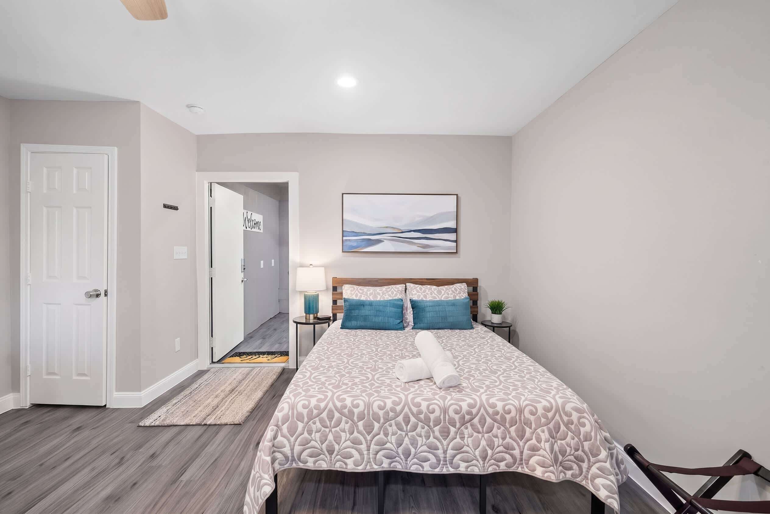 A bedroom with a bed, a nightstand, a lamp, a framed picture on the wall, and a door.