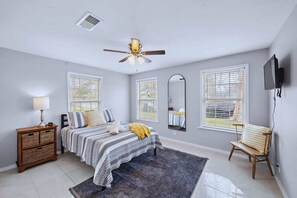 A bedroom with a bed, bedside table, lamp, and a ceiling fan.