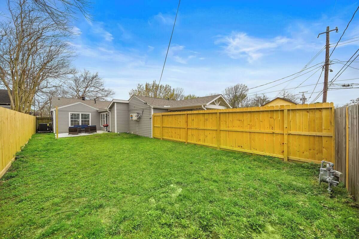 A residential backyard with a wooden fence, a lawn, and a house with a garage.