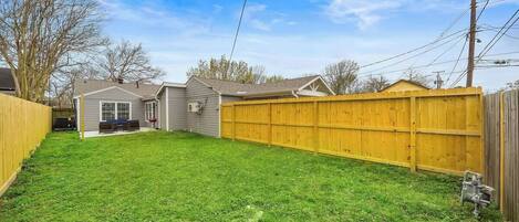 A residential backyard with a wooden fence, a lawn, and a house with a garage.