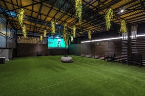An indoor space with artificial grass, hanging plants, a large screen, and seating. - 1HOTEL (Shizuoka)