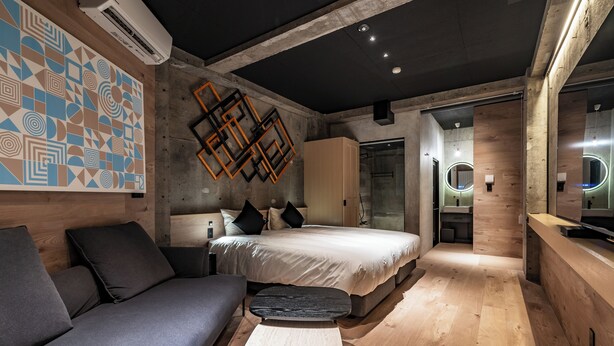 A modern bedroom with a large bed, a sofa, a small table, and a geometric wall decoration. - 1HOTEL (Shizuoka)