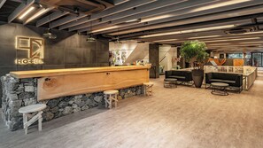 Zona de recepción de hotel con mostrador de madera, pared de piedra y área de descanso.