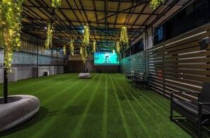 An indoor space with artificial grass, hanging plants, and a projection screen. - 1HOTEL (Shizuoka)